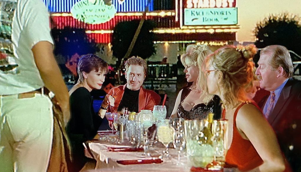 Alle sieben Hauptfiguren sitzen an einem gedeckten Tisch